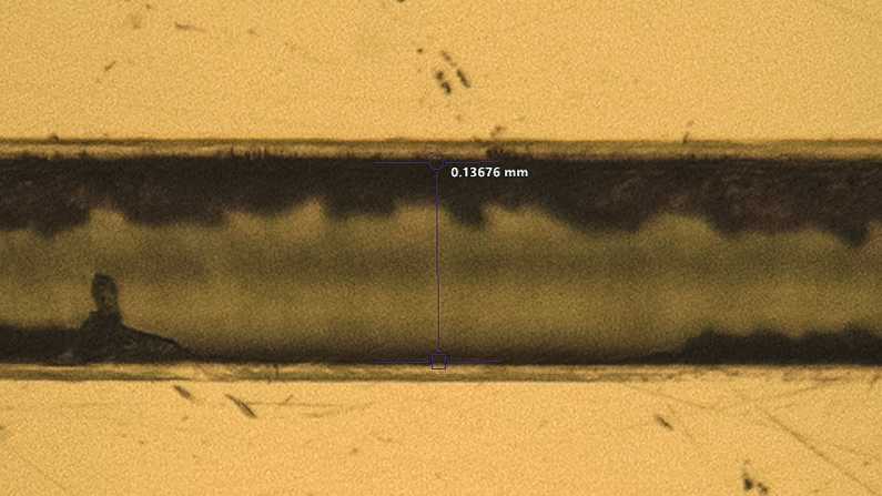 Close-up of a micromilled microfluidic channel that measures 0.13676 millimeters in width at the center. The channel is defined but has a pronounced burr.