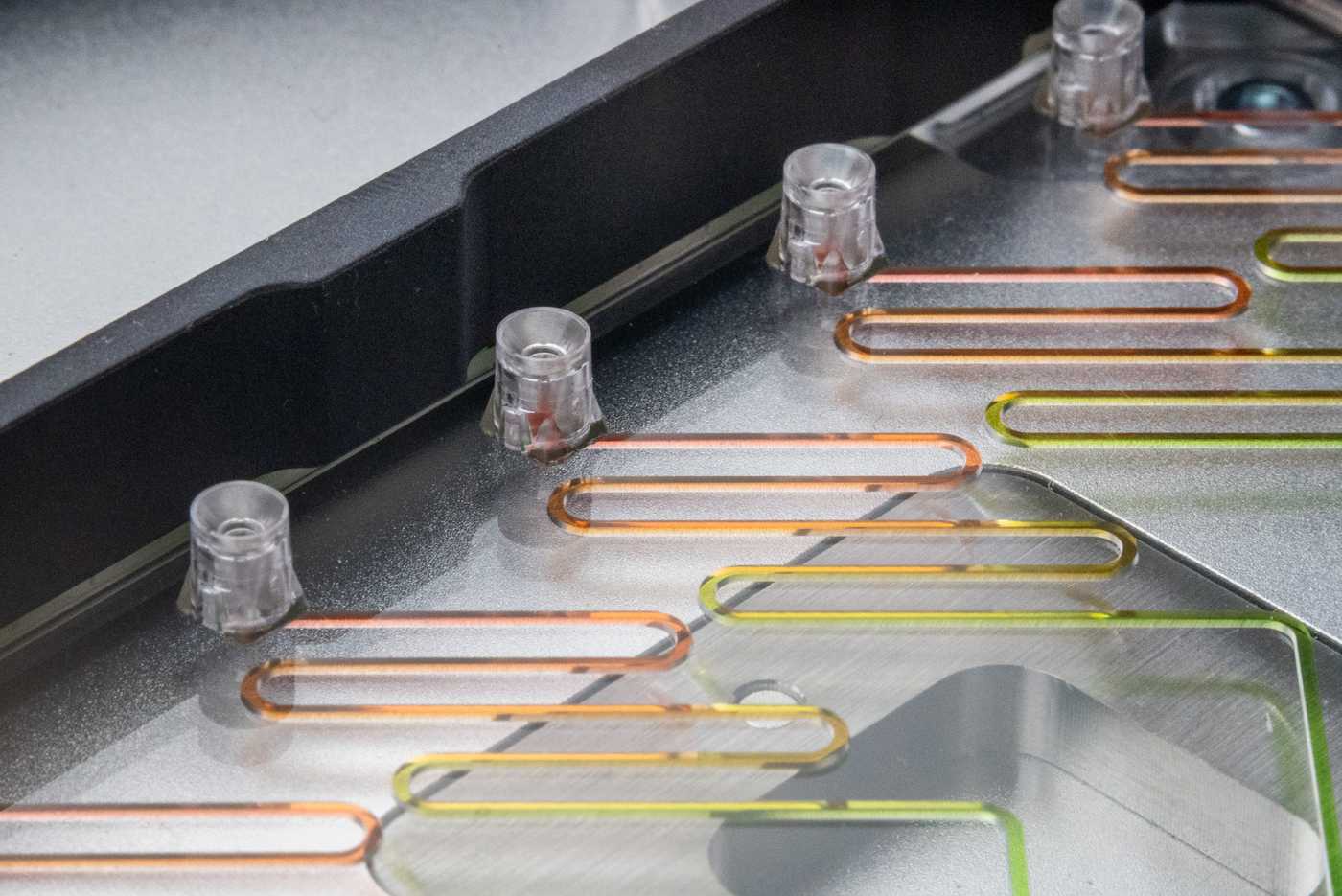 A microfluidic device with an SLAS adapter placed on the deck of an automated liquid handler. The microfluidic device has multiple pipette interfaces along one edge connected to meandering channels filled with multiple colored fluids.